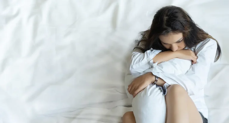 Najpogostejše duševne motnje – ženska, ki žalostno sedi na postelji in objema blazino.