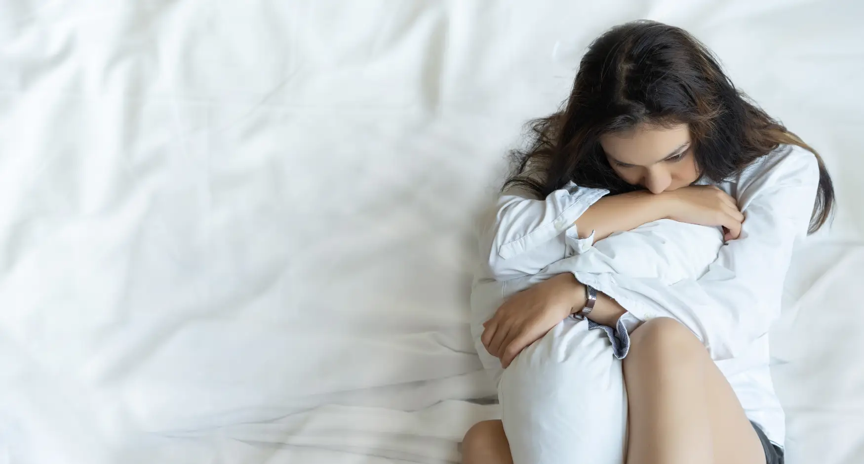 Najpogostejše duševne motnje – ženska, ki žalostno sedi na postelji in objema blazino.