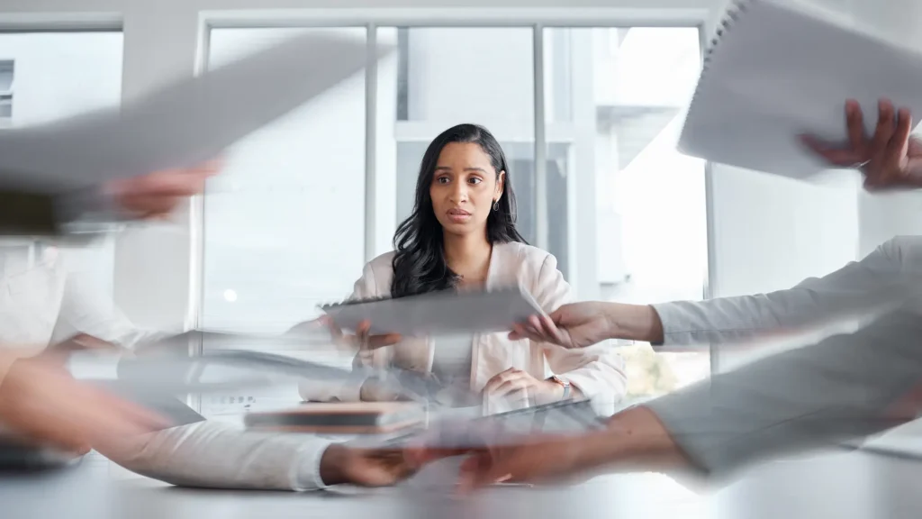 Ženska z zmedenim in zaskrbljenim izrazom sedi med množico hitrih, nepovezanih dražljajev – simbol občutka odtujenosti in preobremenjenosti.