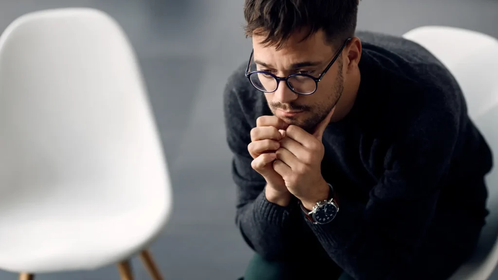 Moški s sklonjeno glavo in zaskrbljenim izrazom sedi v tišini – simbol notranje stiske in duševne napetosti.