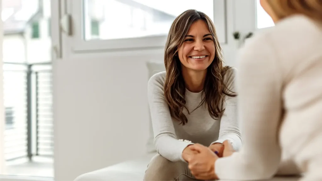 Ženska se nasmejano pogovarja s terapevtko med svetovanjem, kar simbolizira odprt pogovor in podporo za duševno zdravje