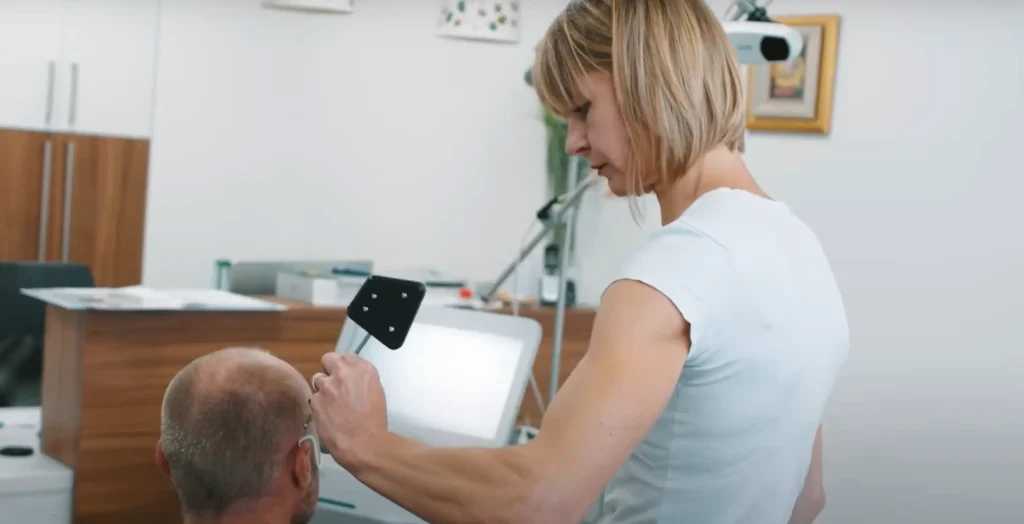 Fizioterapevtka izvaja TPS terapijo na pacientu s pomočjo naprave Neurolith v terapevtskem prostoru