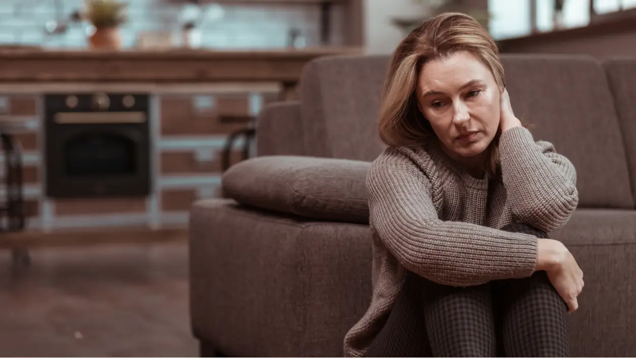 Kako premagati depresijo – ženska z žalostnim izrazom sedi ob kavču in razmišlja o stiski